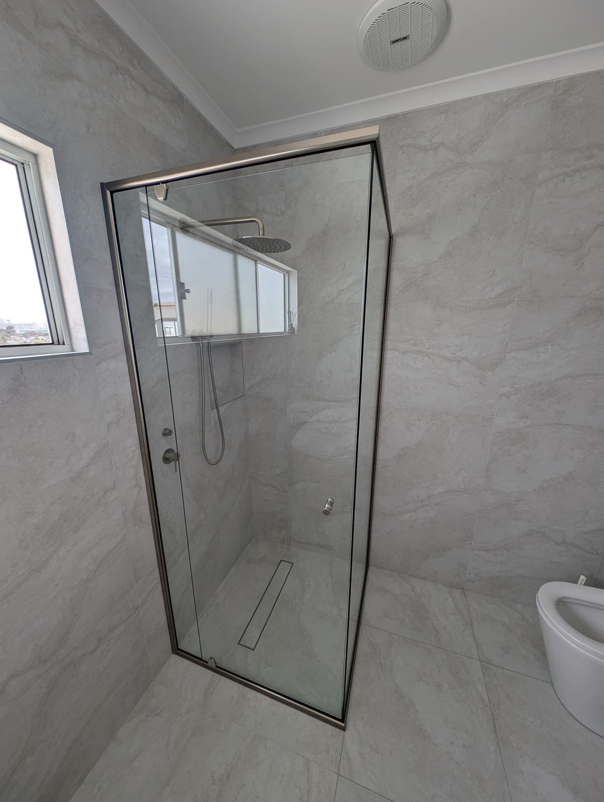 Semi-frameless corner shower screen with a slim brushed nickel frame and pivot door, marble-look tiles