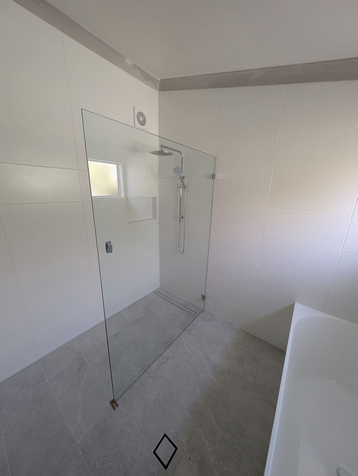Single fixed frameless glass panel in a white-tiled walk-in shower with a grey stone floor